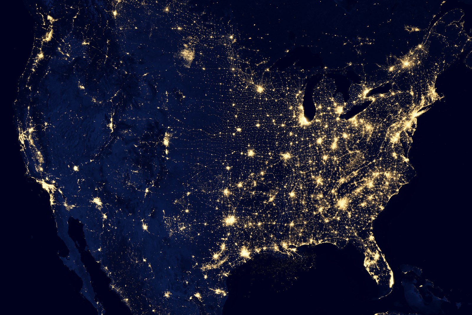 A satellite night view of the United States showing cities glowing in warm yellow against the dark land — a real picture of light pollution.